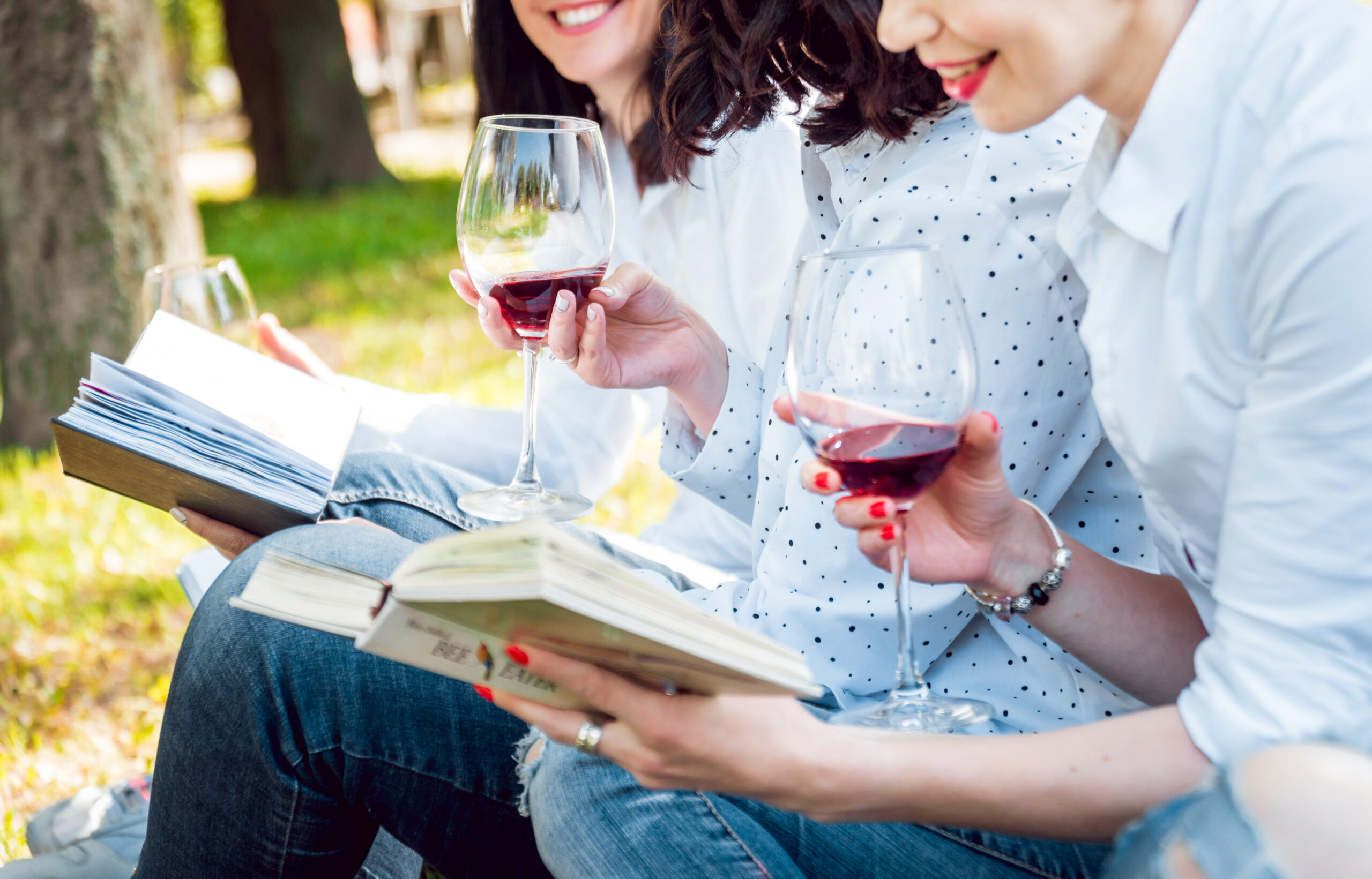 Young women with glasses of red wine and books in the park.